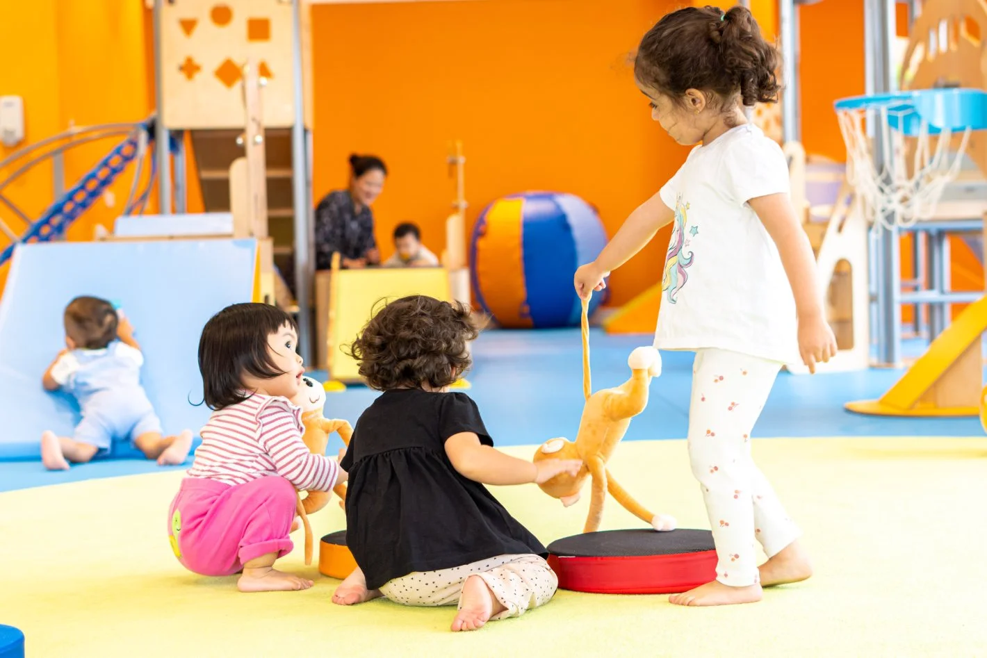 Three toddlers playing together on the floor of a bright play room